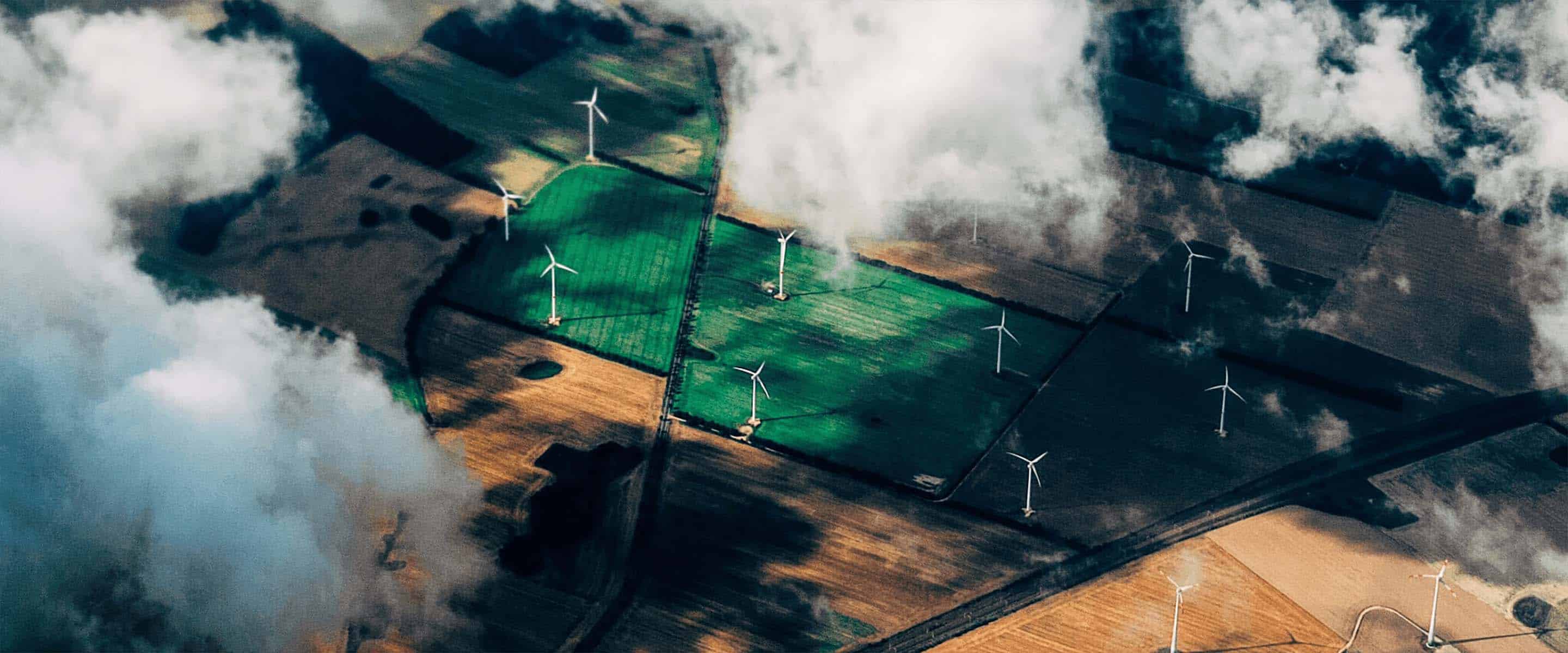 A cloudy aerial view of wind turbines on farmland.